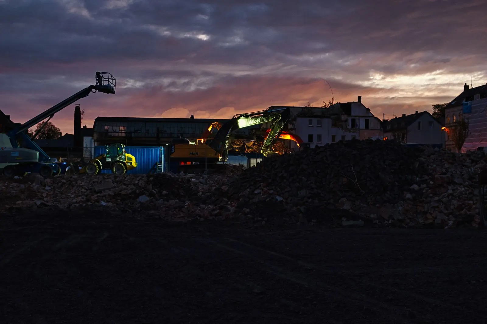 Baustelle in der Dämmerung mit Bagger, Radlader und Arbeitsbühne